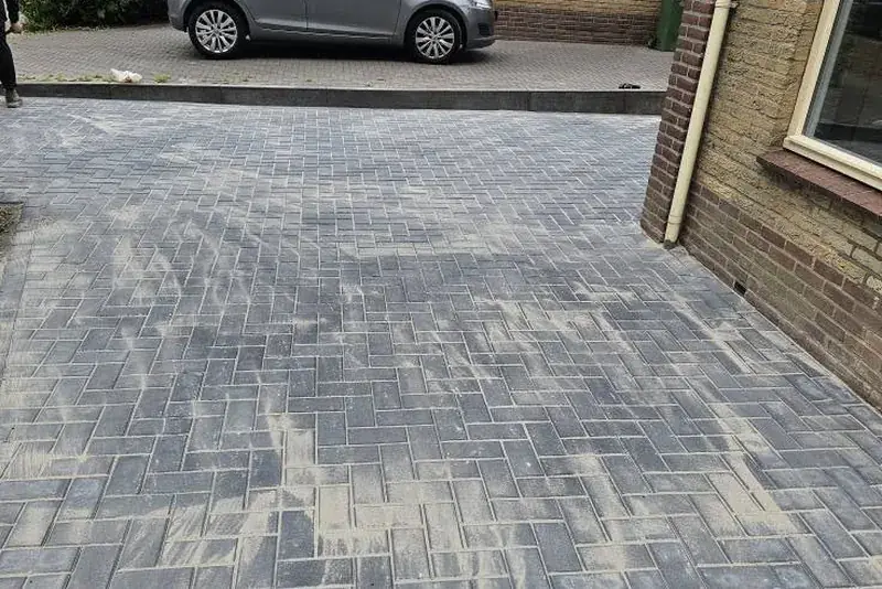 Nieuwe oprit in grijze klinkers, gelegd in keperverband, naast een woonhuis