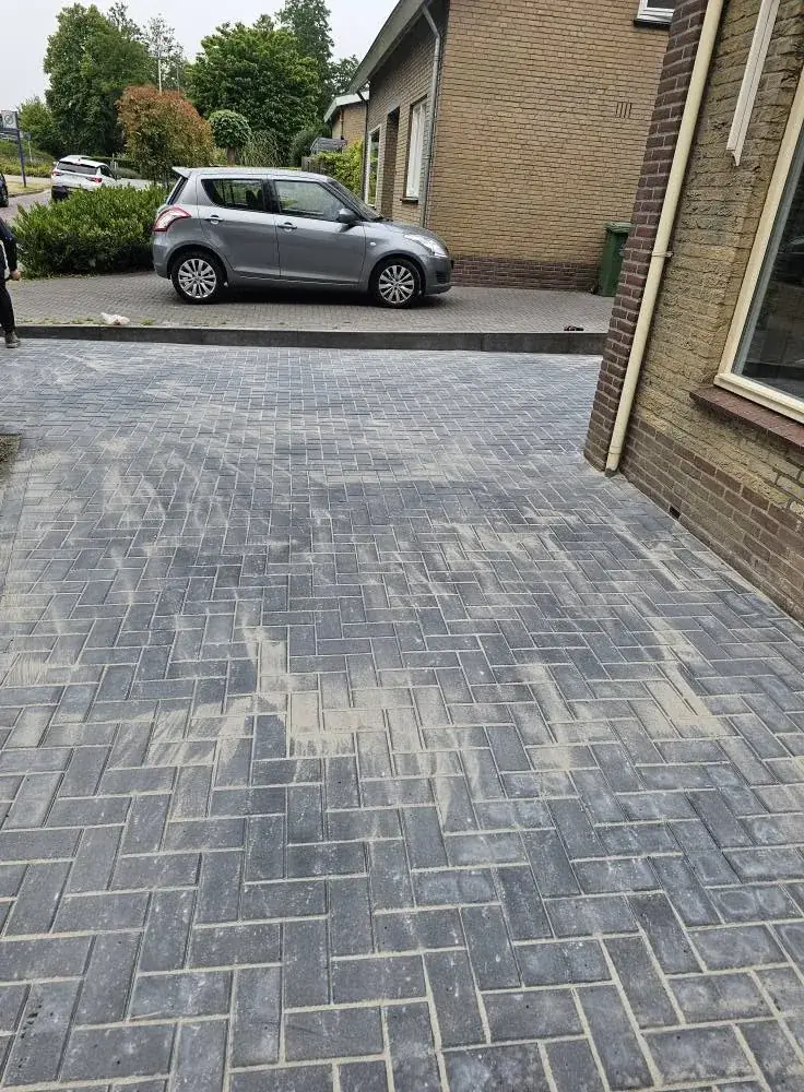 Nieuwe oprit in grijze klinkers, gelegd in keperverband, naast een woonhuis