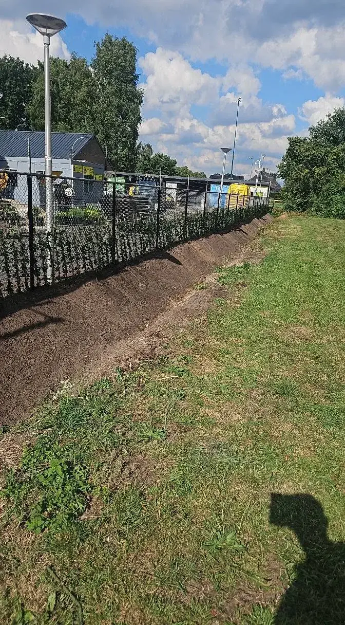 Zwart gaashekwerk langs een pas afgewerkt talud, met grondwerk over de volle lengte