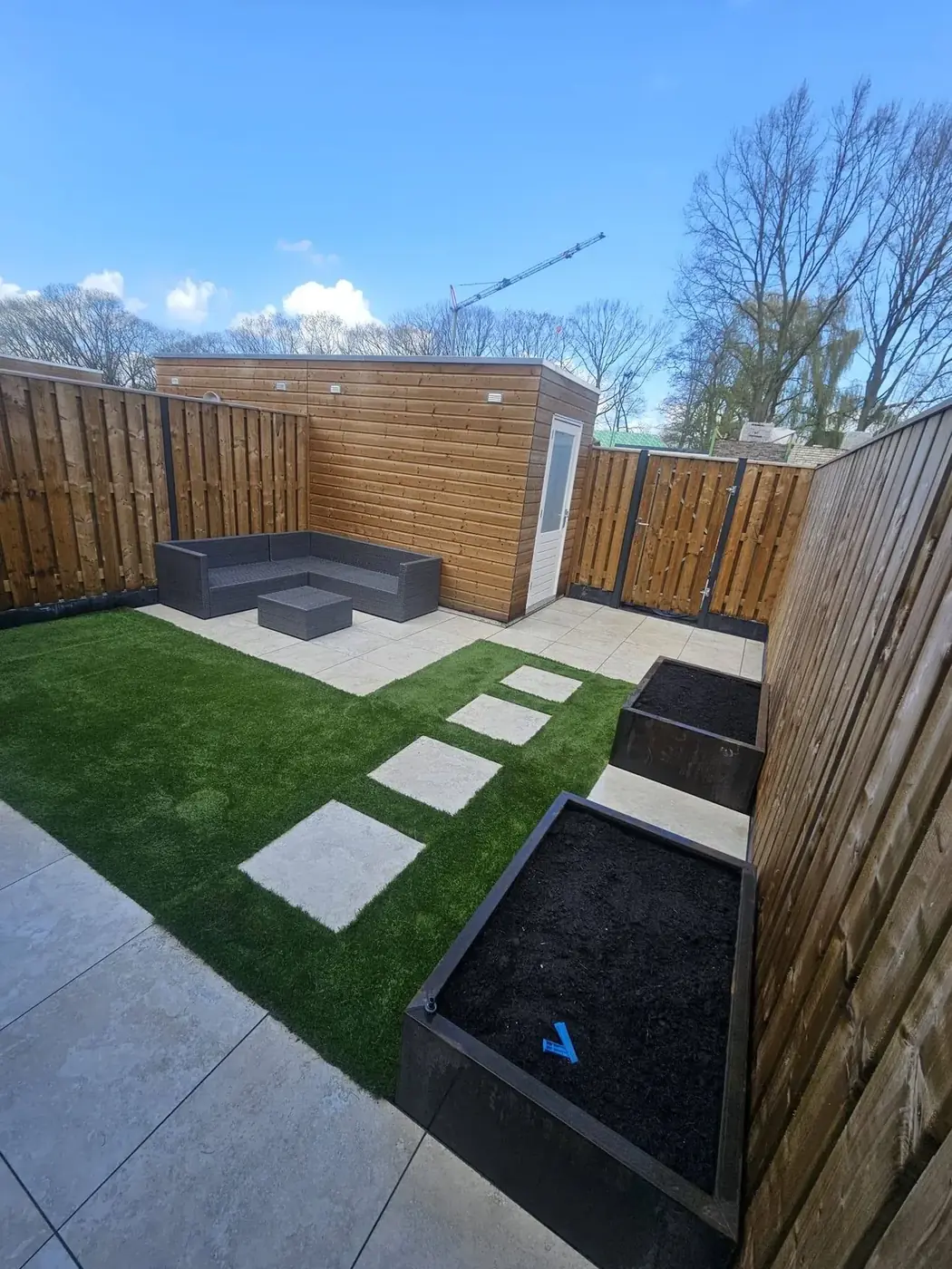 Door Voske Tuinprojecten aangelegde achtertuin met kunstgras, keramisch terras en plantenbakken van cortenstaal