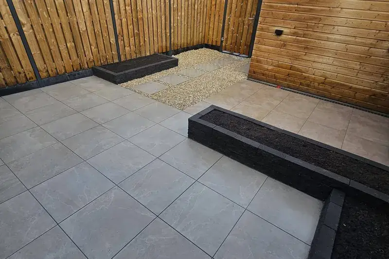Achtertuin met keramisch terras, borders met stapelblokken, grindpad met stapstenen en een houten schutting