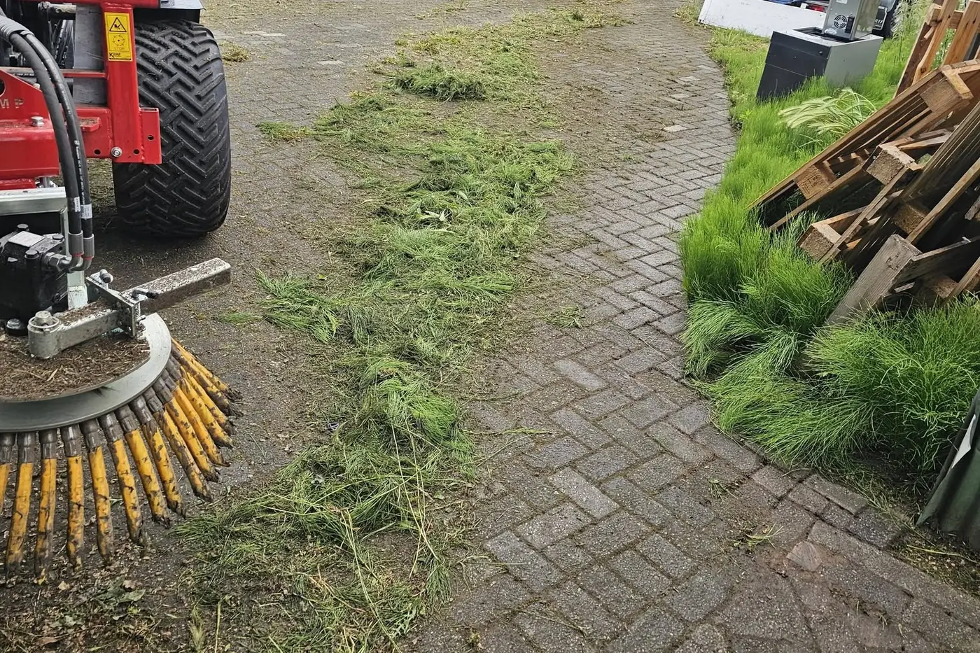 Machinaal onkruid borstelen van een klinkerpad, met het losgeborstelde gras ernaast