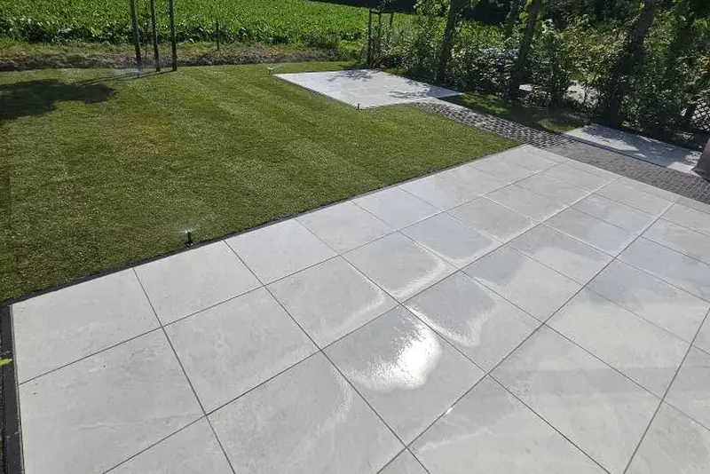Gerenoveerde tuin met nieuw keramisch terras en strak gemaaid gazon, met uitzicht op het veld